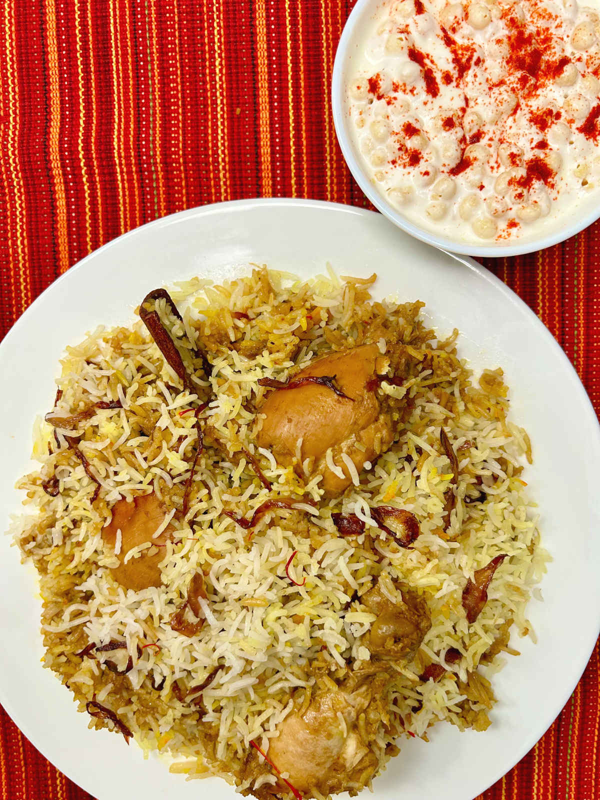 plate of jerk chicken dum biryani with a bowl of raita on the side