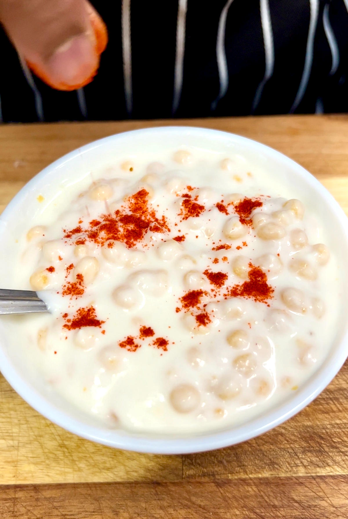 sprinkling red chili powder onto a bowl of raita