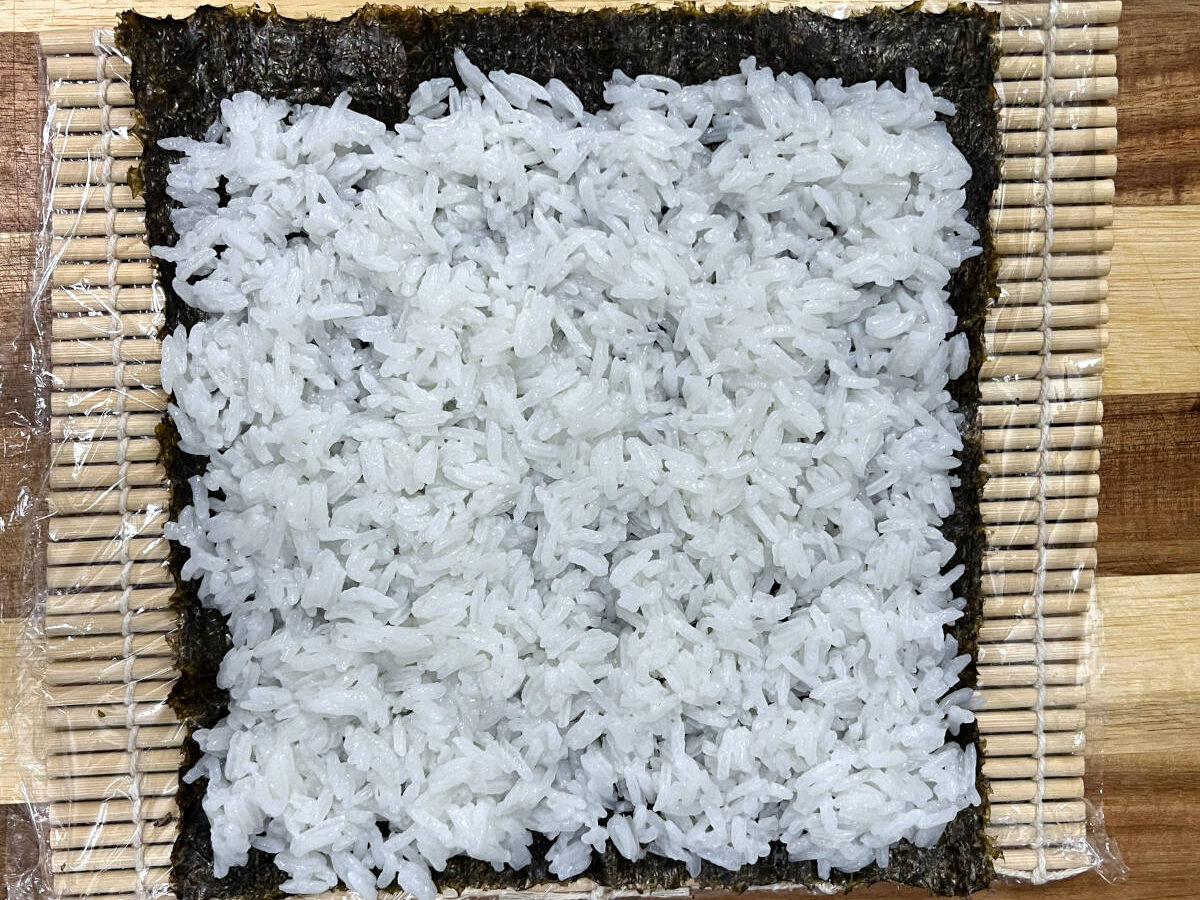 rice placed over a nori sheet on a bamboo mat