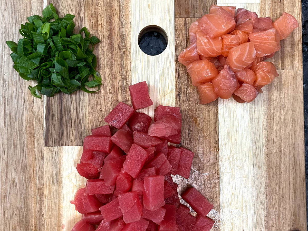 chopped green onions, salmon and tuna on a cutting board