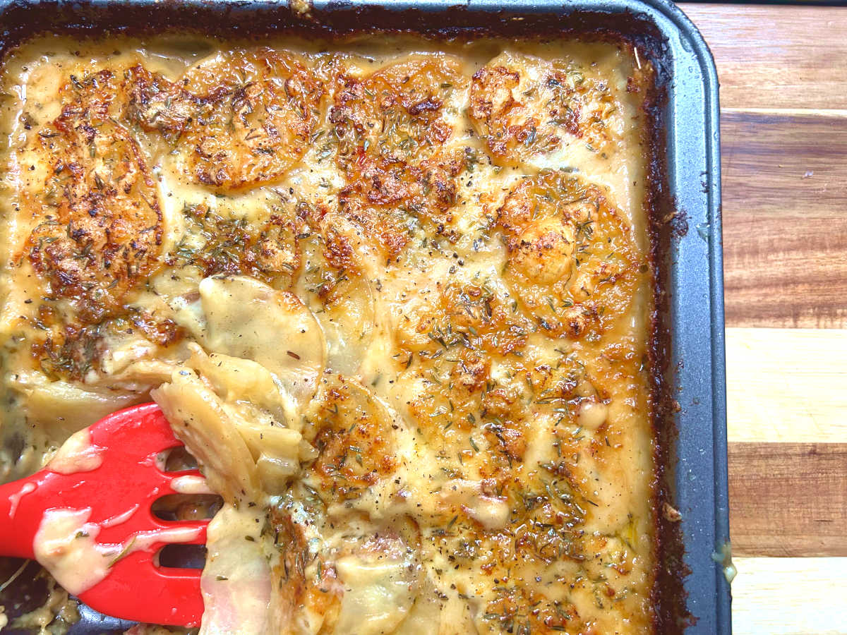 scooping a slice of potatoes au gratin from the baking tray
