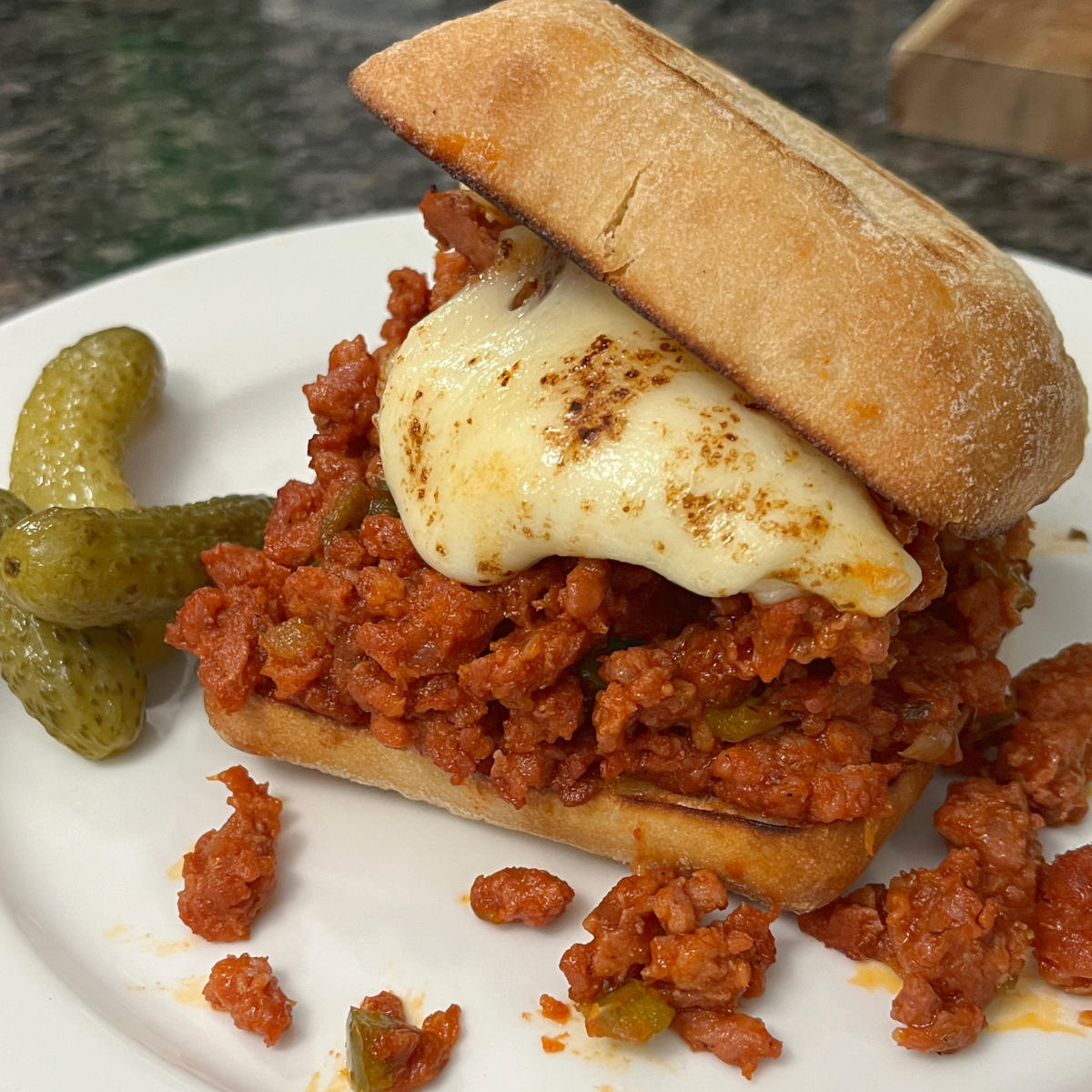 Sloppy joes on a plate with pickles on the side