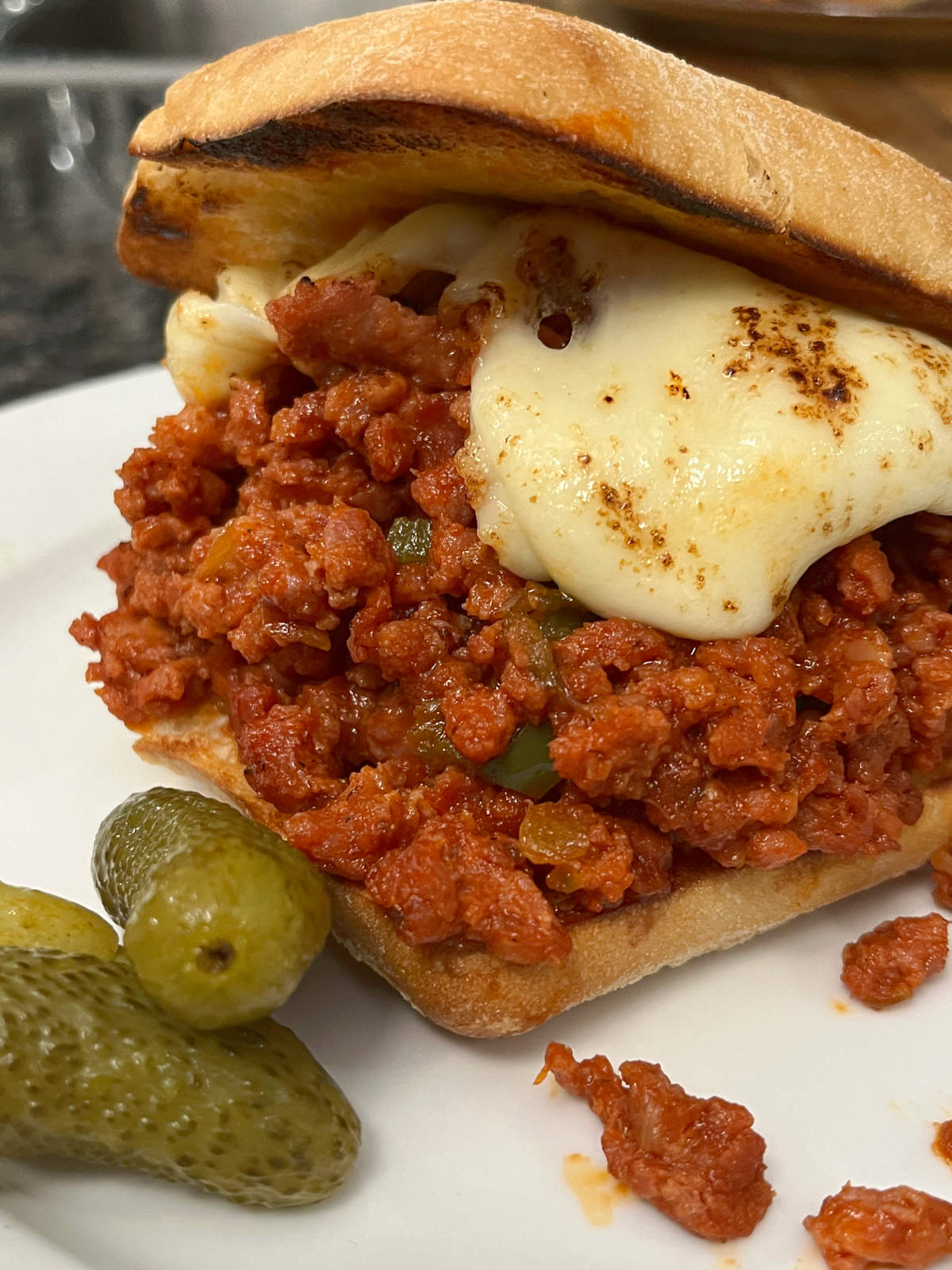 Sloppy joes on a plate with pickles on the side