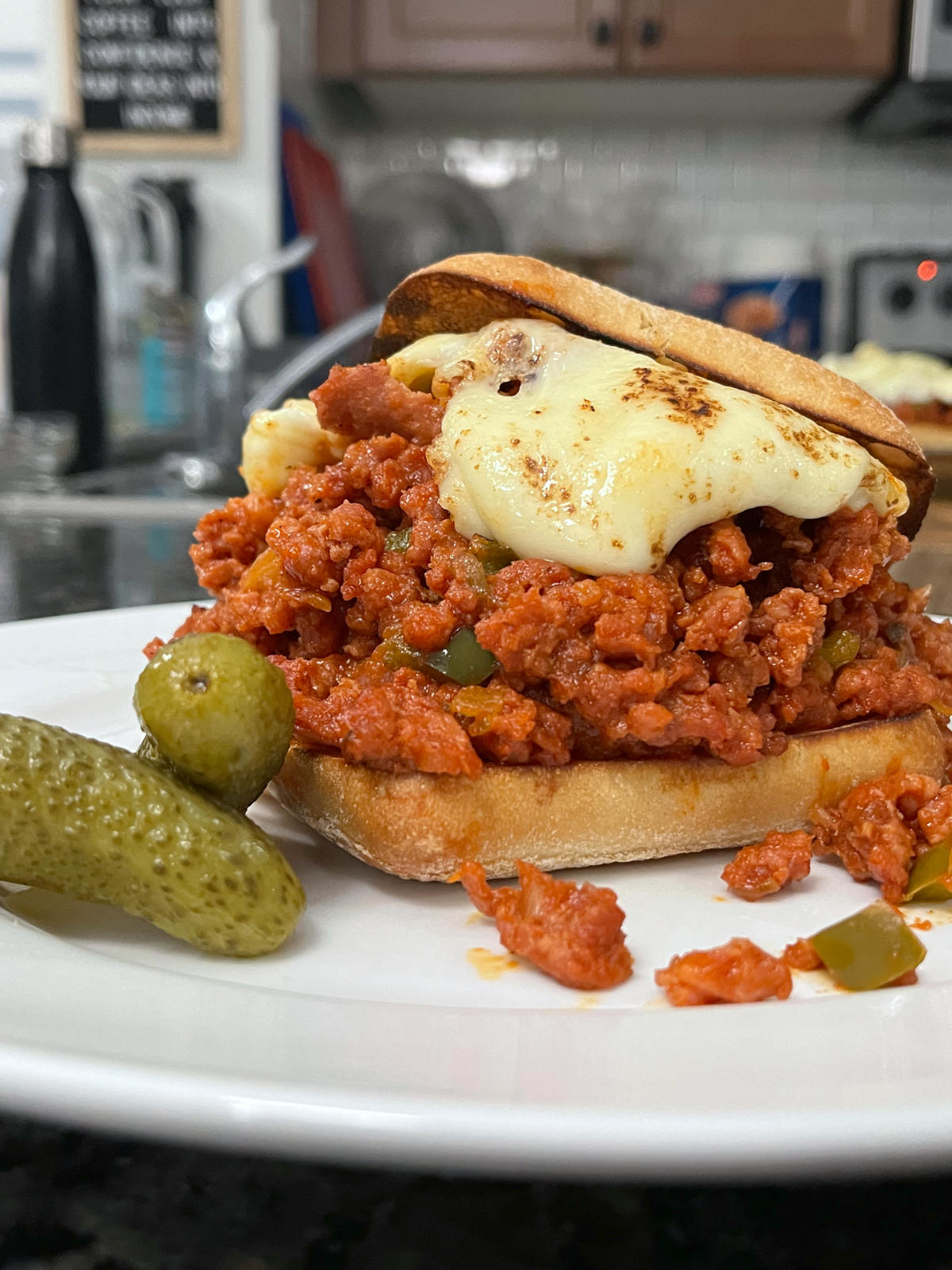 Sloppy joes on a plate with pickles on the side