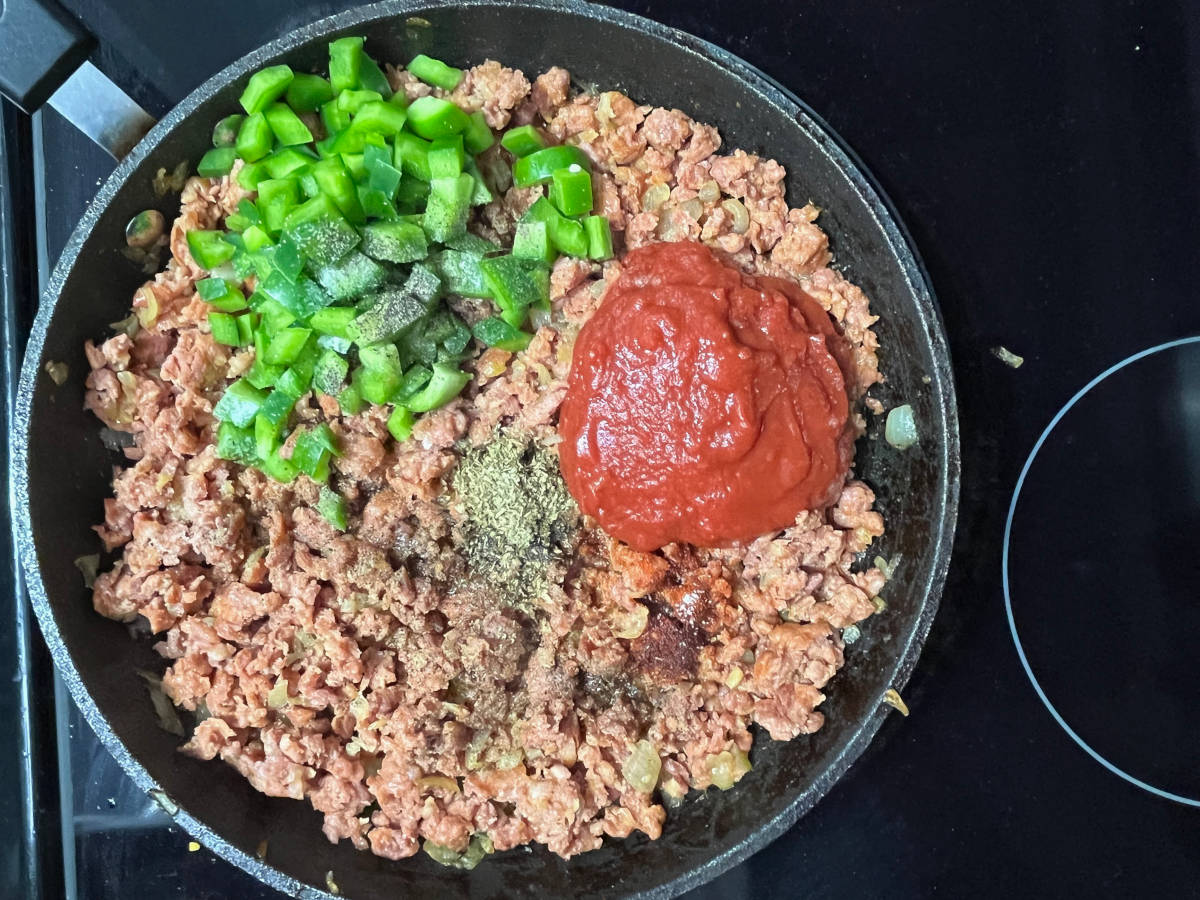 Adding bell peppers and crushed tomatoes to the pan