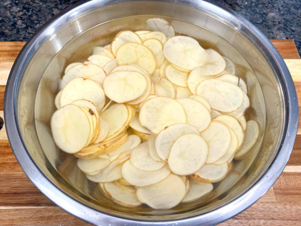 thinly sliced potatoes in a bowl of water