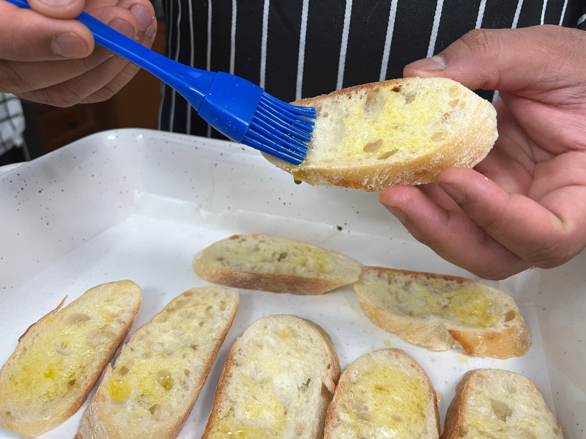 Brushing olive oil on a slice of baguette