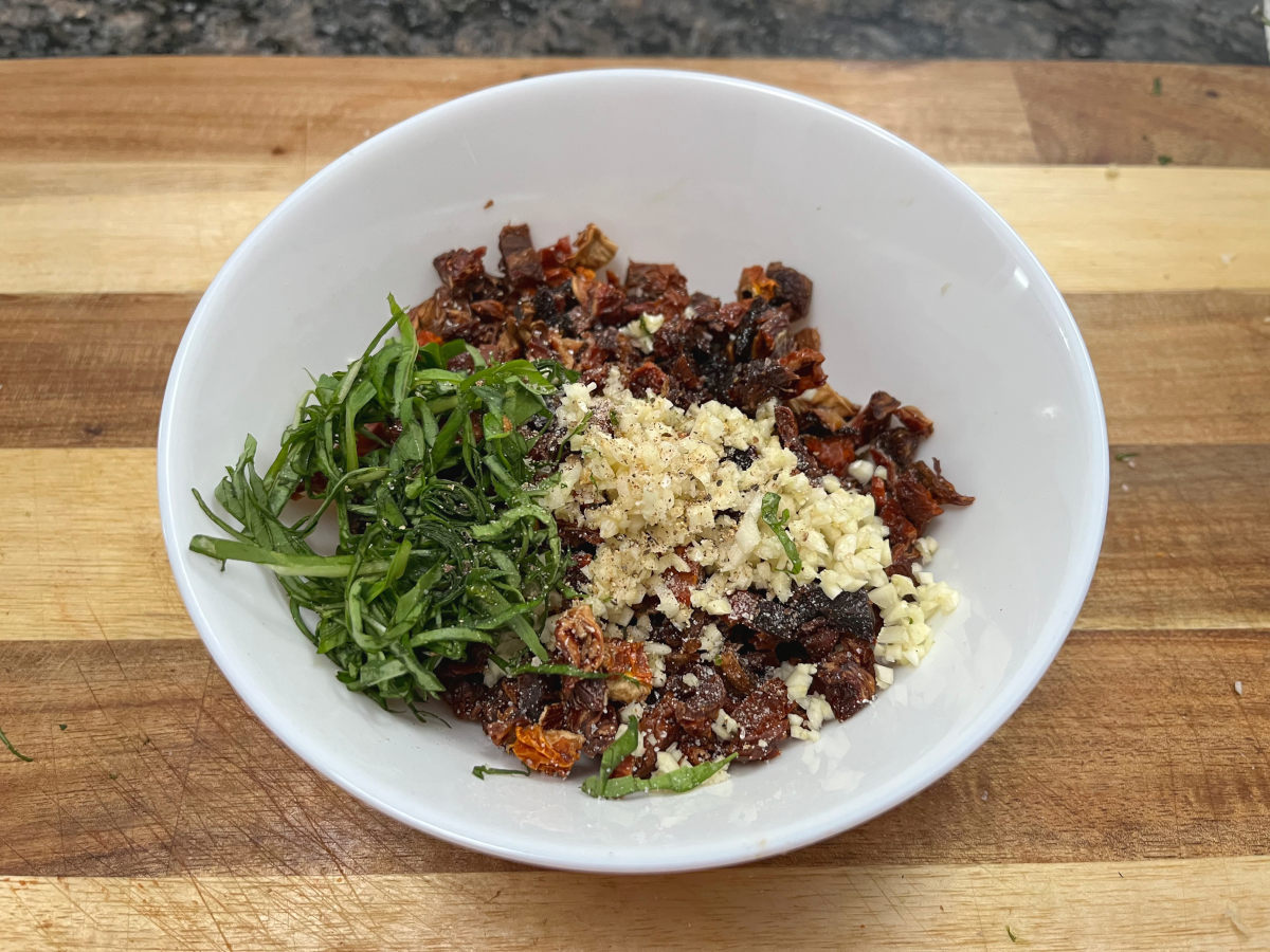 Mixture of sun-dried tomatoes, minced garlic, fresh basil and extra-virgin olive oil in a bowl