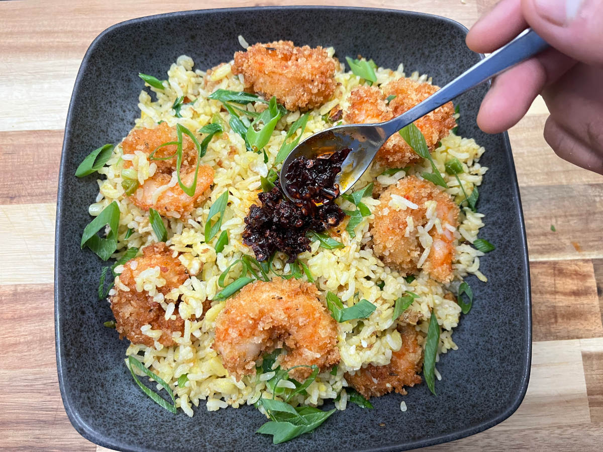 Golden fried rice with Cajun shrimp in a bowl and a spoon of chili oil