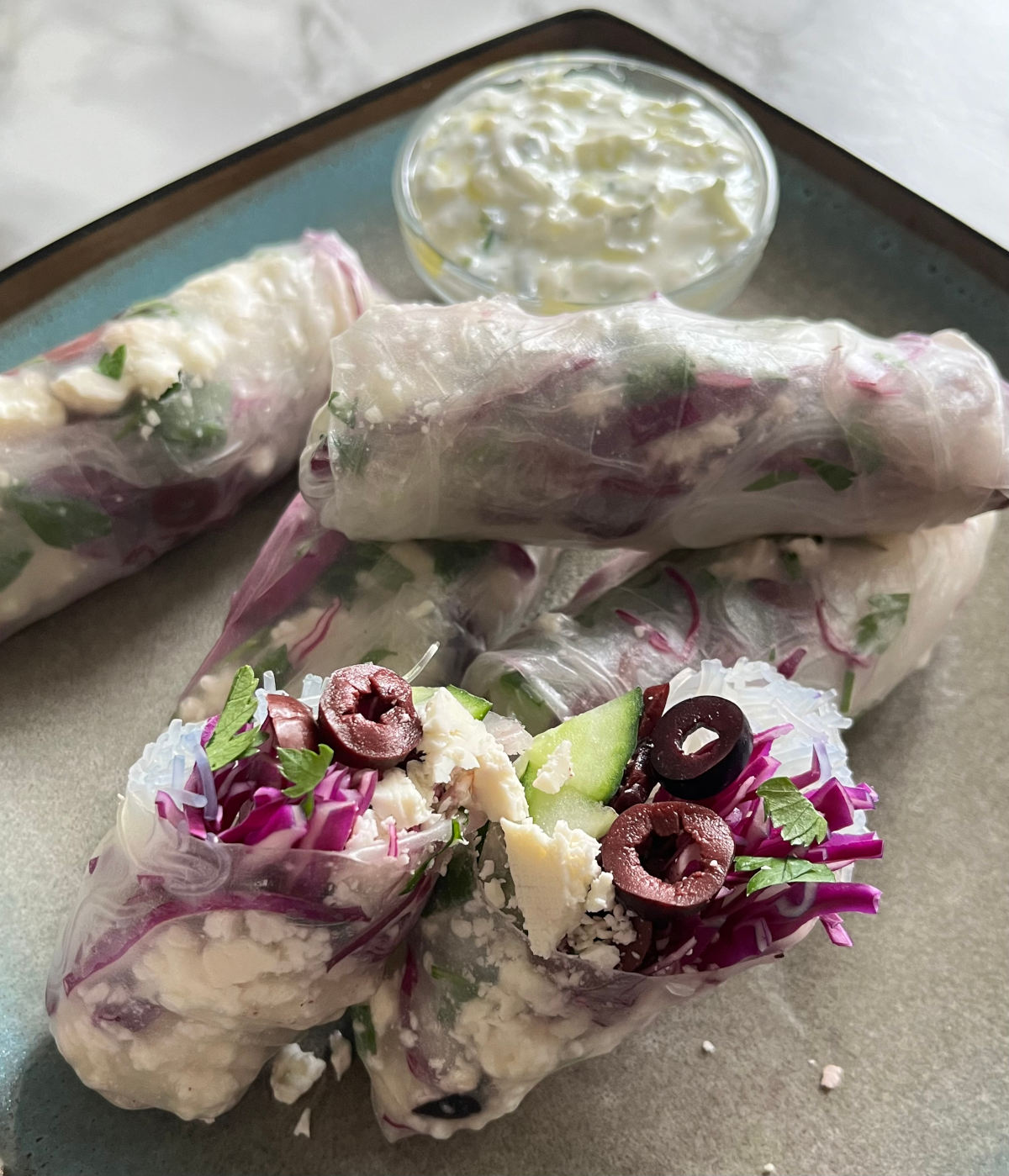 Five Mediterranean spring rolls on a plate with a small bowl of tzatziki sauce