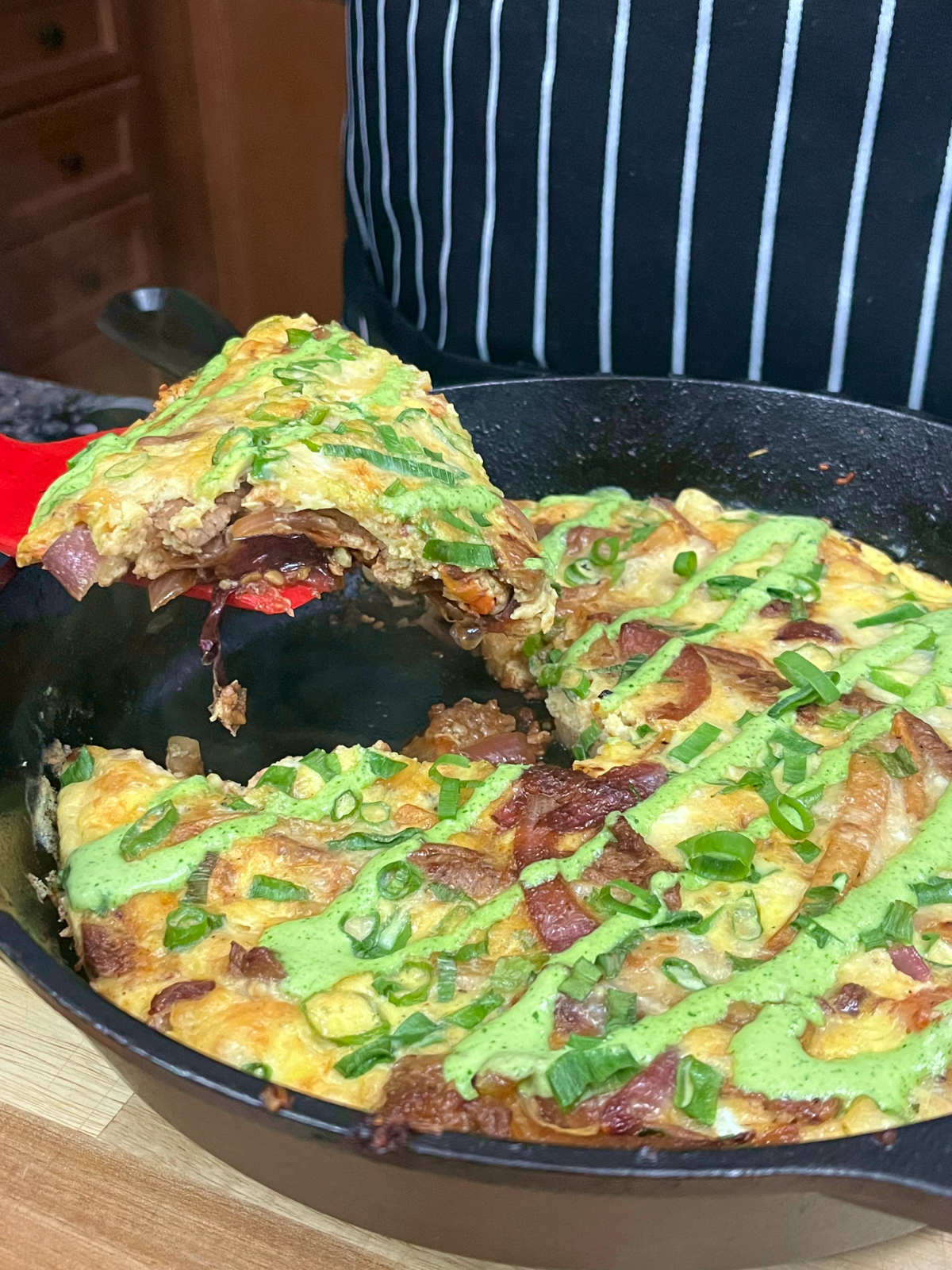 scooping out a slice of lomo saltado frittata from the skillet with a red spatula