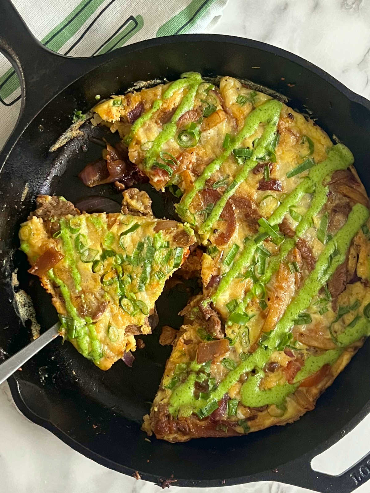cut out slice of lomo saltado frittata in a skillet with a fork