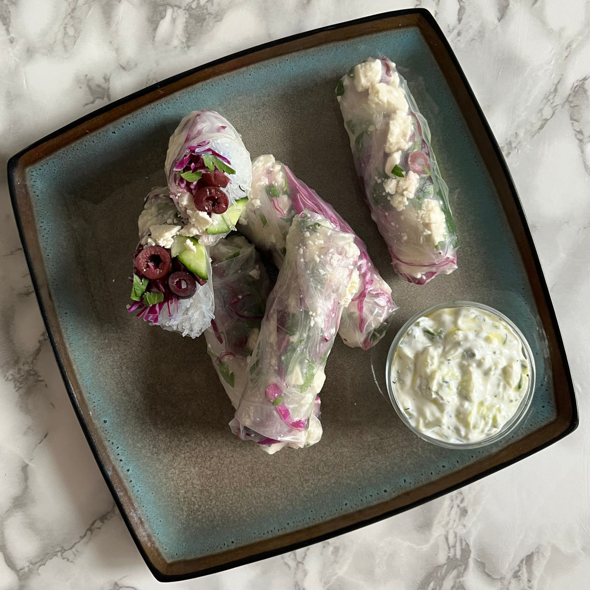 Five Mediterranean spring rolls on a plate with a small bowl of tzatziki sauce