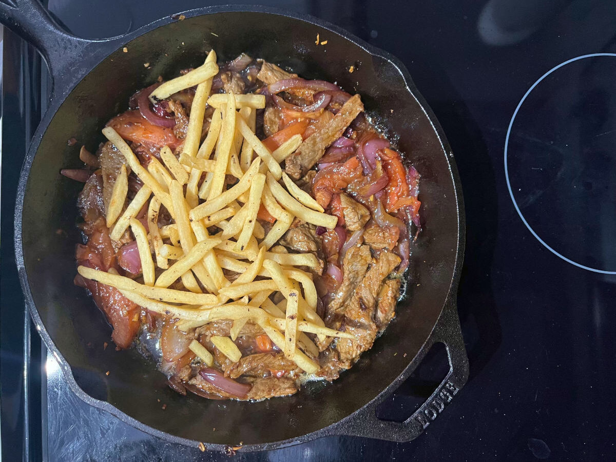 beef, garlic, onions, tomatoes and French fries in a skillet