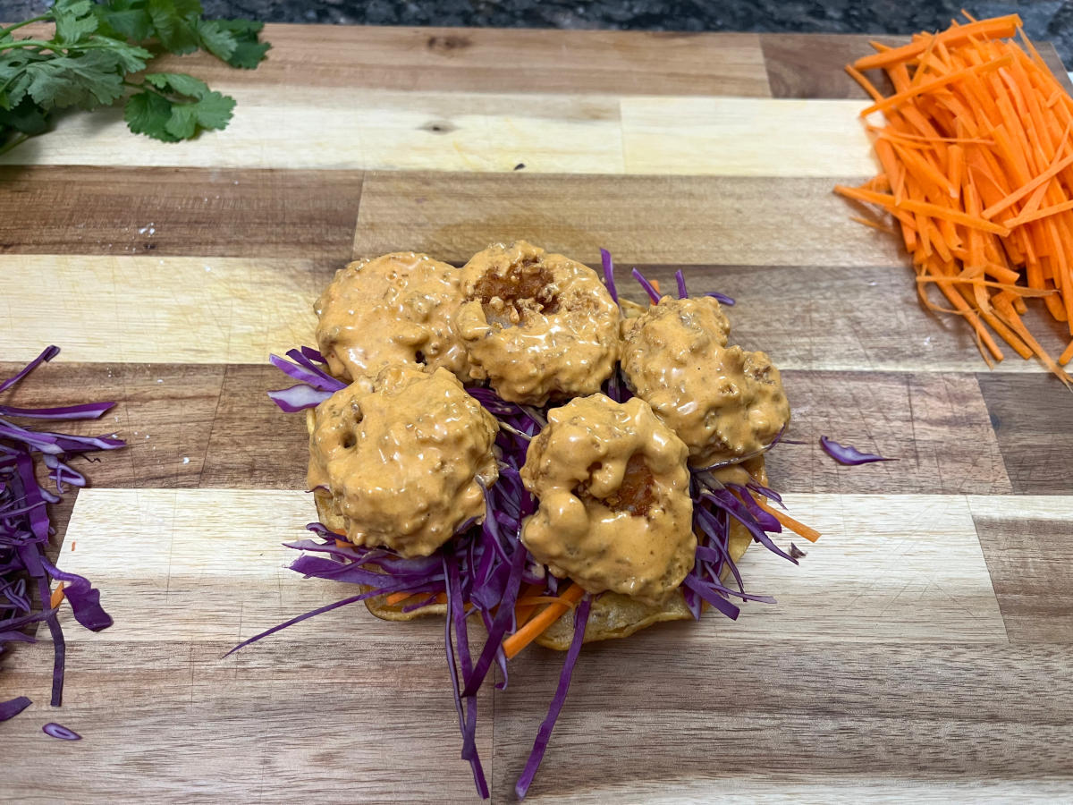 Serving the prawns coated with sauce over some veggies on a tostada