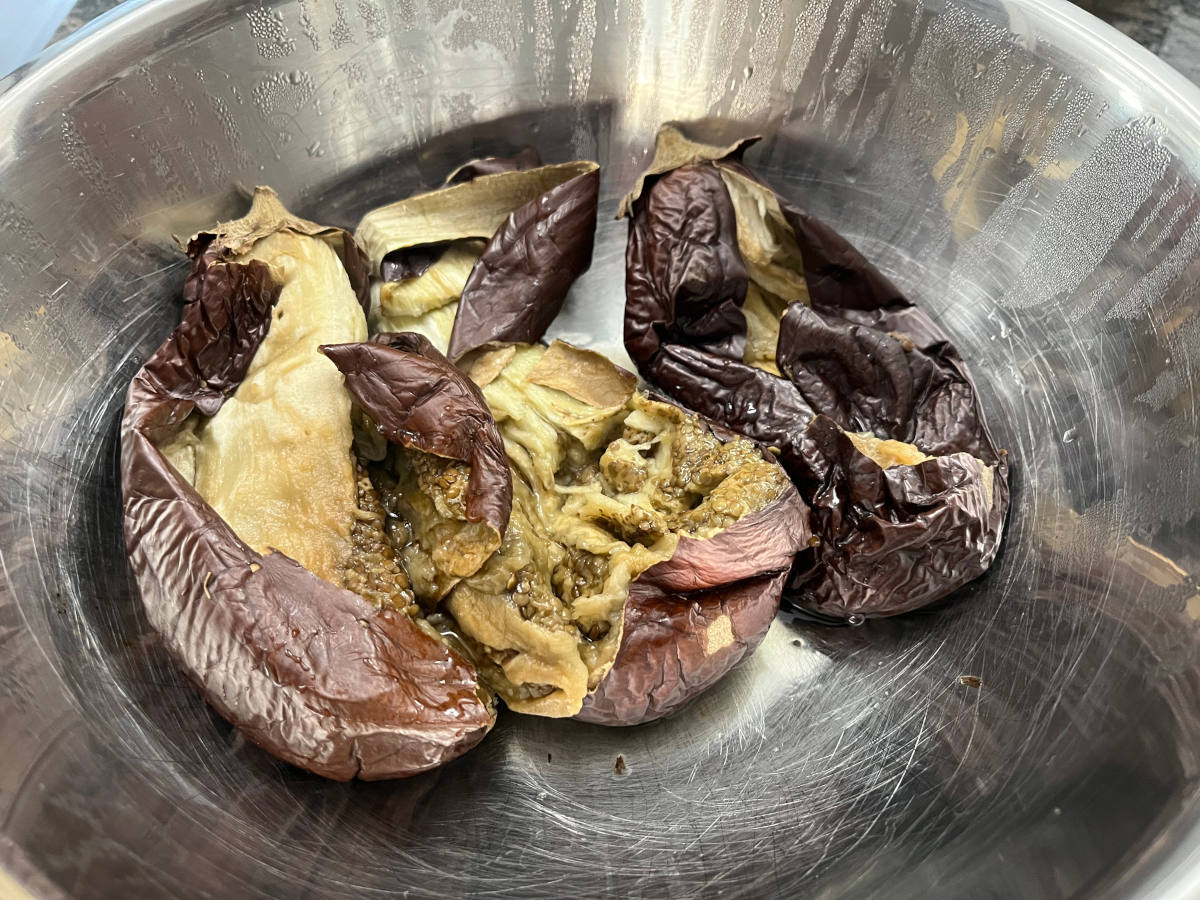 Three partially peeled eggplants in a bowl