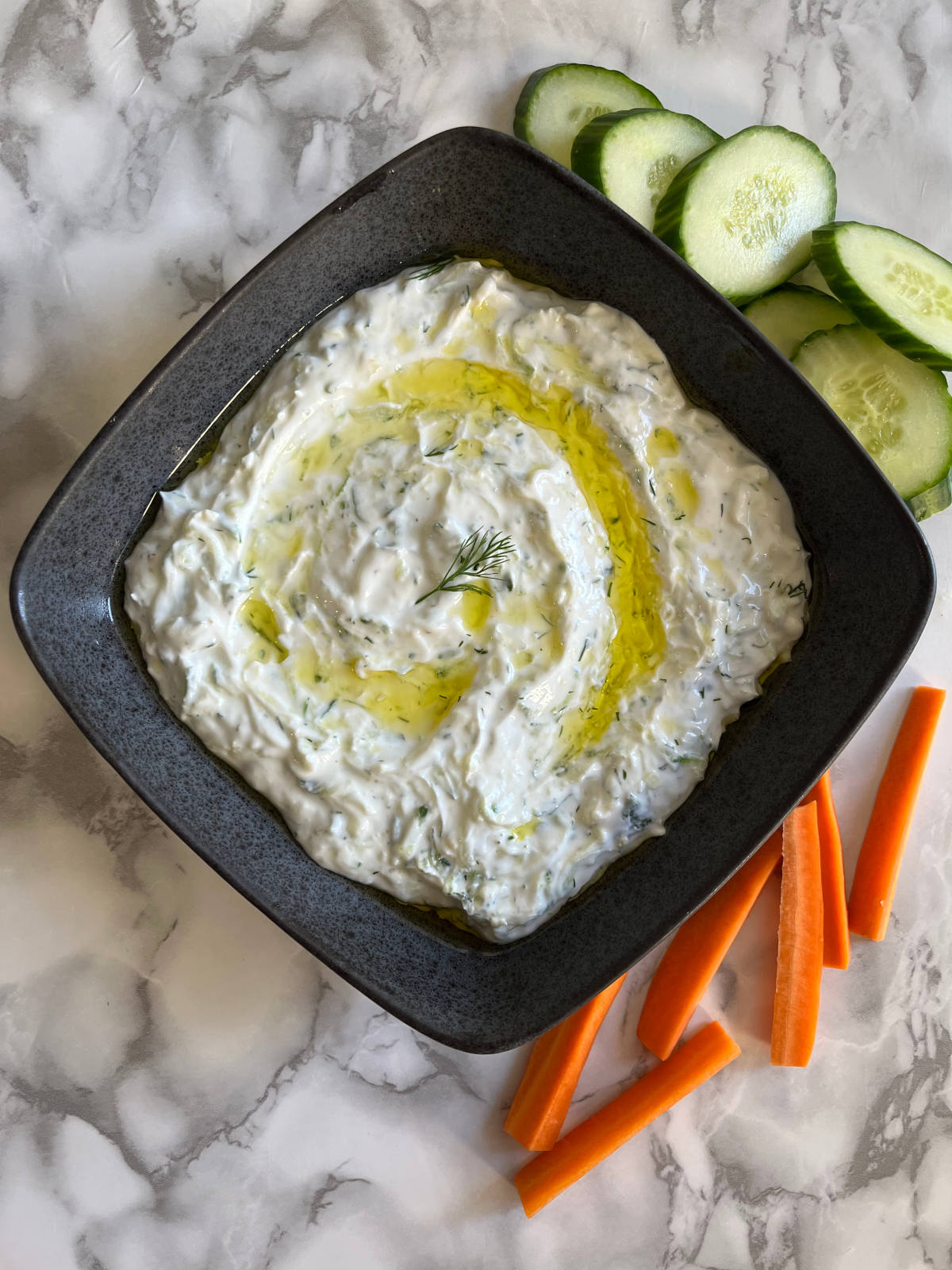 Tzatziki in a bowl with sliced cucumbers and carrots on the side