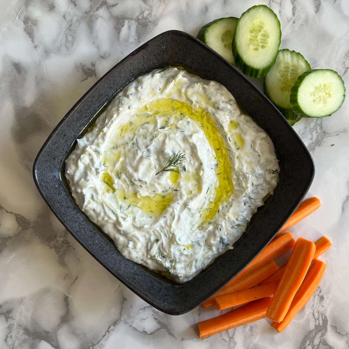 Tzatziki in a bowl with sliced cucumbers and carrots on the side