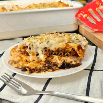 slice of Greek moussaka lasagna with a fork on the side and casserole dish behind