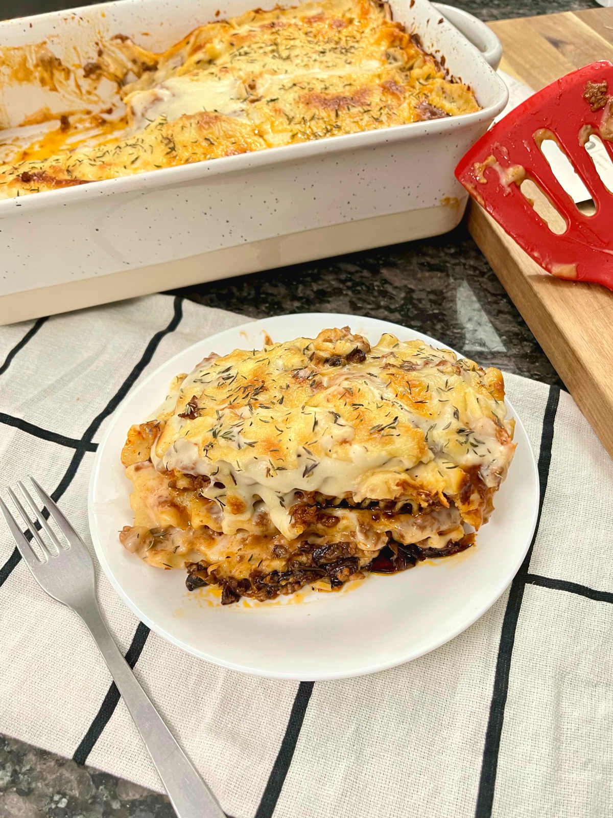 slice of Greek moussaka lasagna with a fork on the side and casserole dish behind