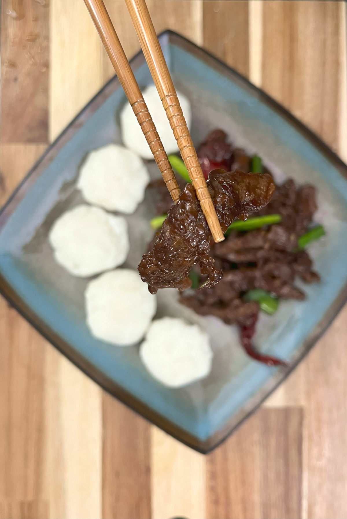 A strip of Mongolian Beef picked up with a pair of Chopsticks, from the plate of Mongolian Beef Ugali