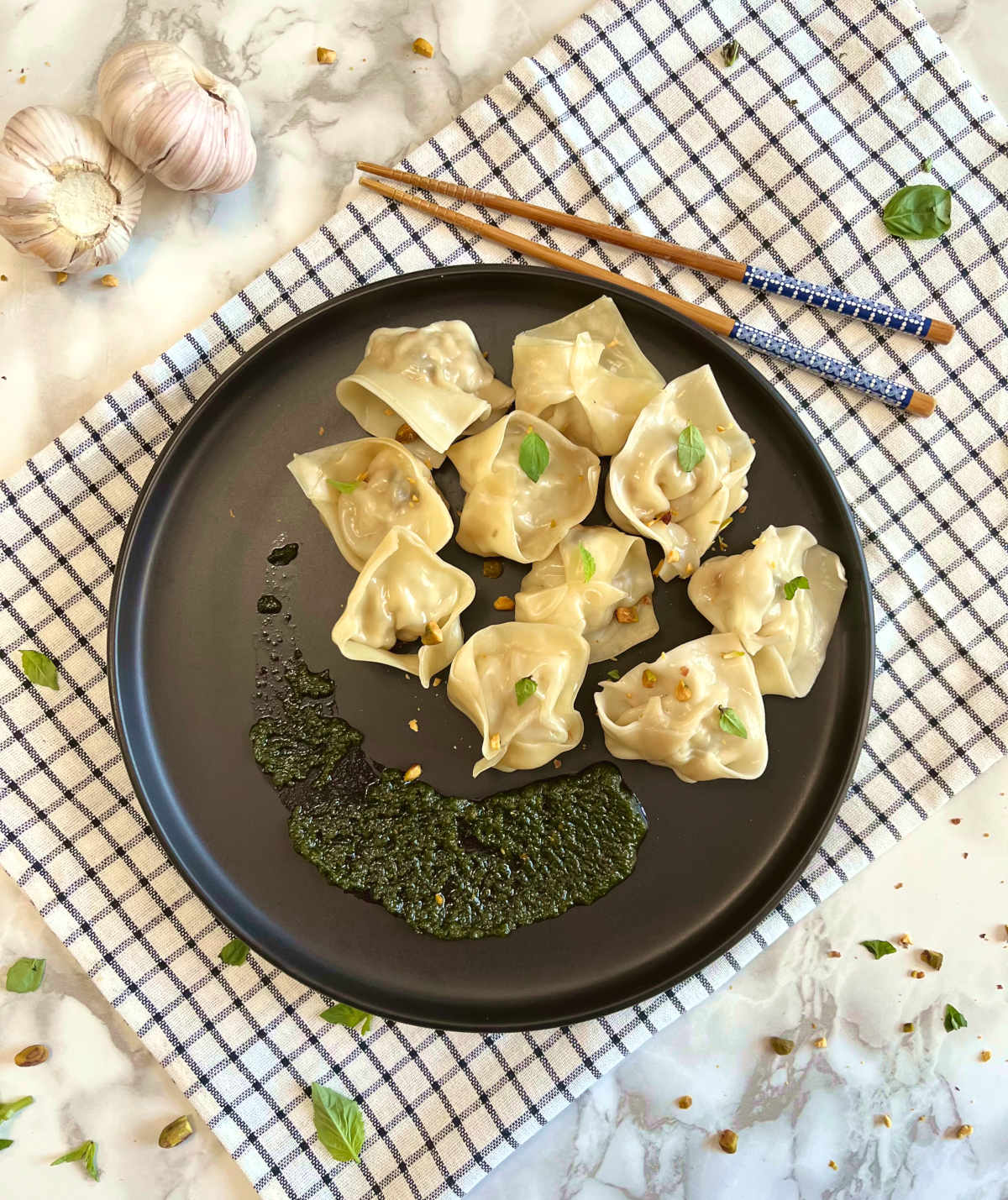 Shrimp wontons in a plate with pesto sauce, and chopsticks on the side