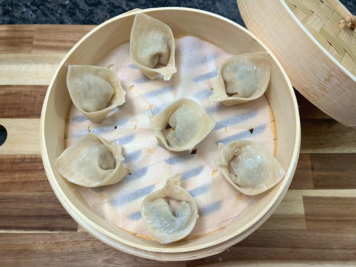 folded wontons placed in a bamboo steamer