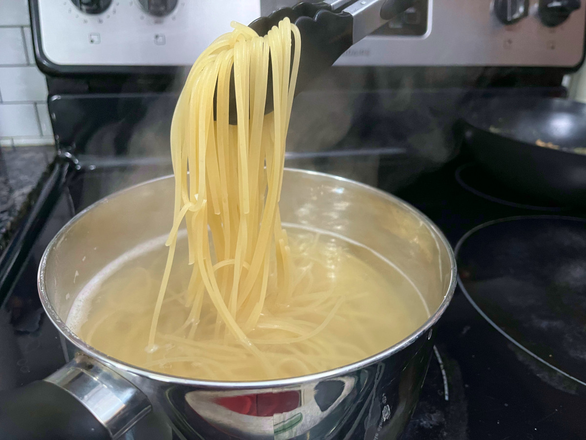 boiled spaghetti picked up by a pair of tongs from a pan