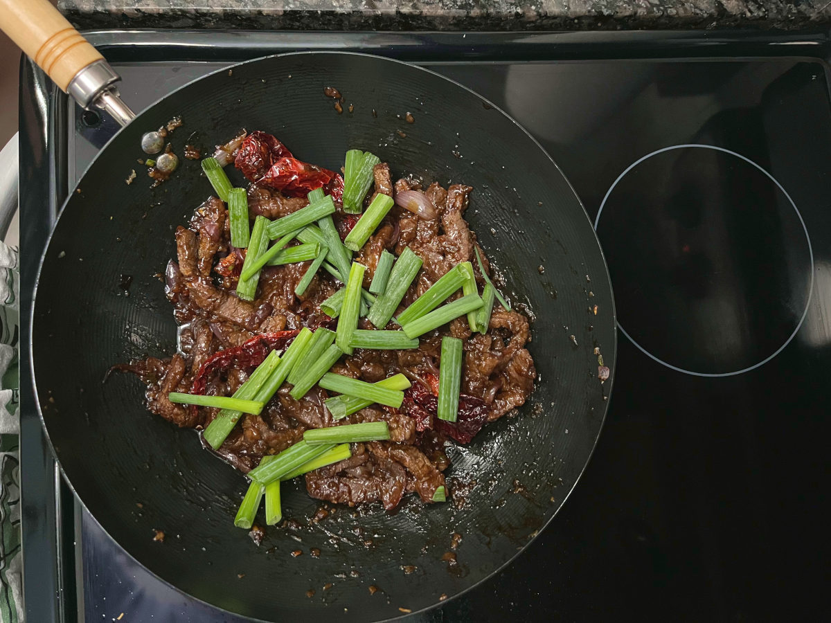 Mongolian beef frying in a wok with spring onions added on top