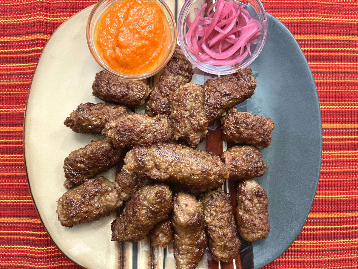 cevapi in a plate with ajvar sauce and picked onions in a bowl