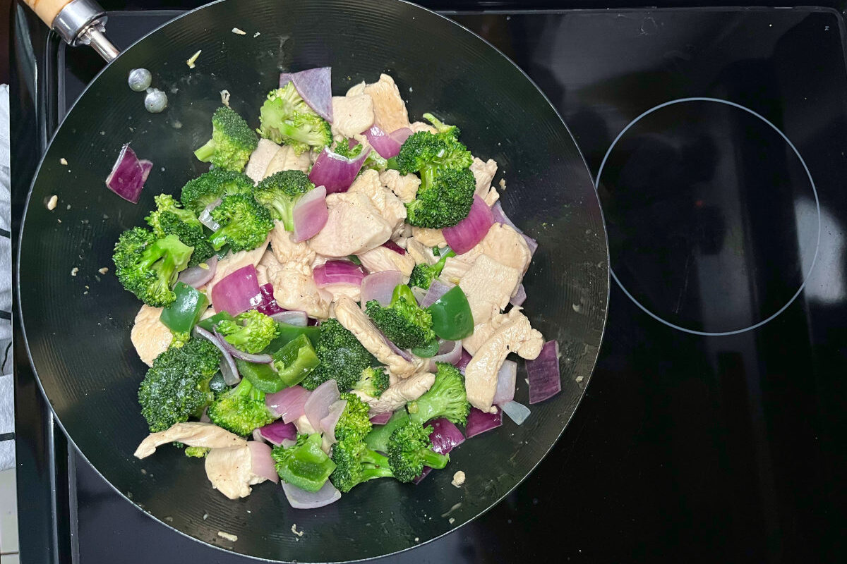 stir frying chicken and veggies in a wok
