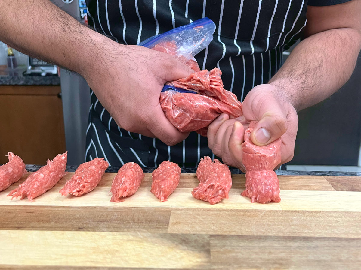 squeezing out ground meat mixture to form a sausage shape