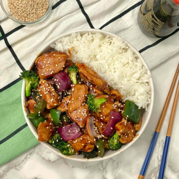 hoisin chicken and broccoli stir-fry with chopsticks, sesame seeds and soy sauce on the side