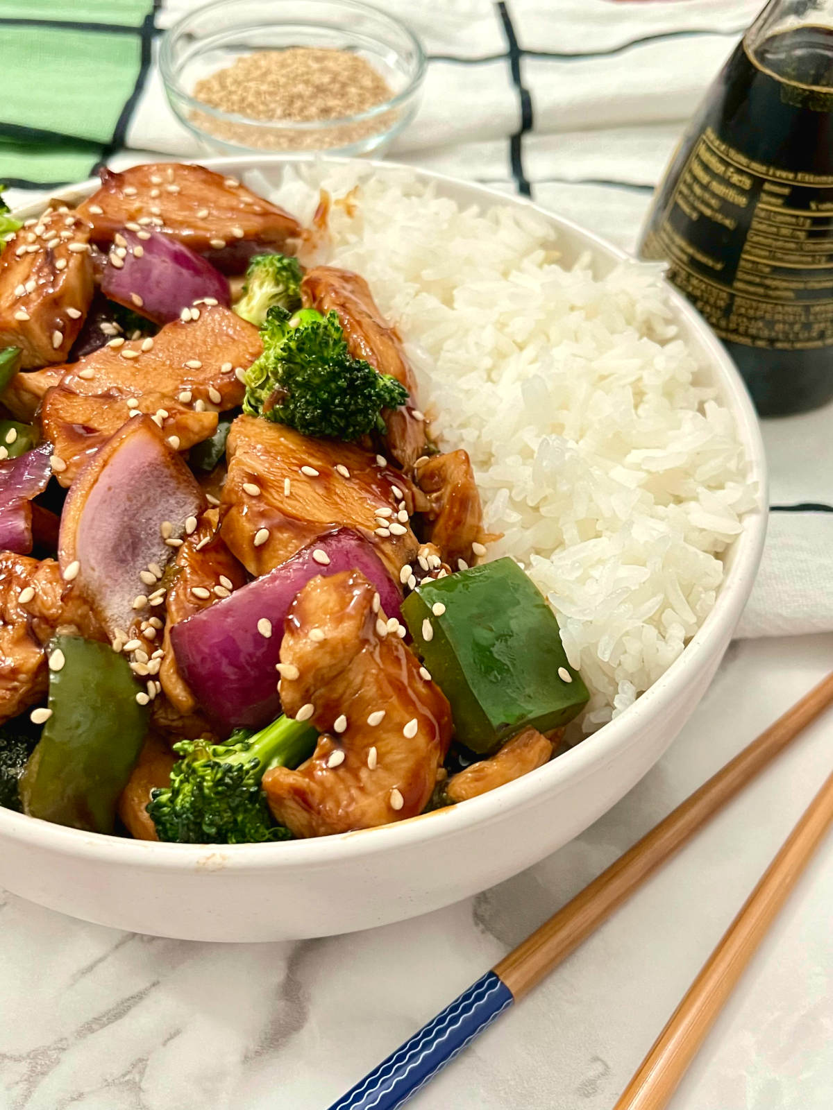 hoisin chicken and broccoli stir-fry with chopsticks, sesame seeds and soy sauce on the side