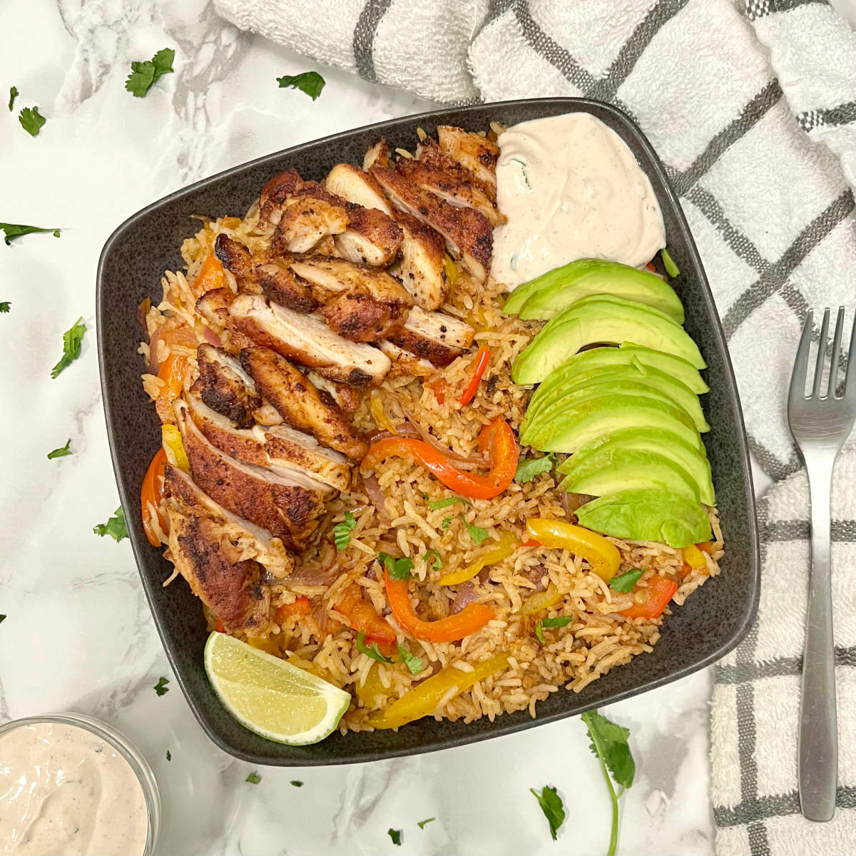 chicken fajita rice bowl with a fork and sour cream sauce on the side