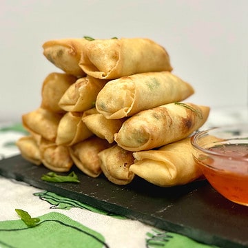 crab rangoon egg rolls stacked on a slate with a sauce on the side