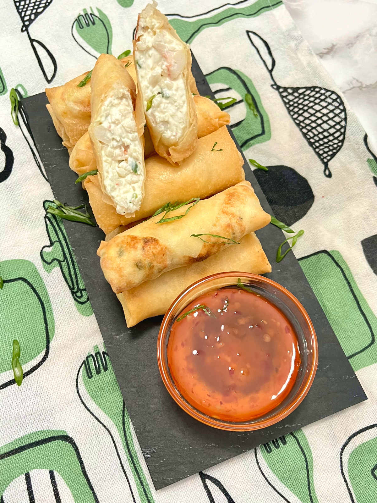 One half cut egg roll on a slate with more egg rolls and a sauce