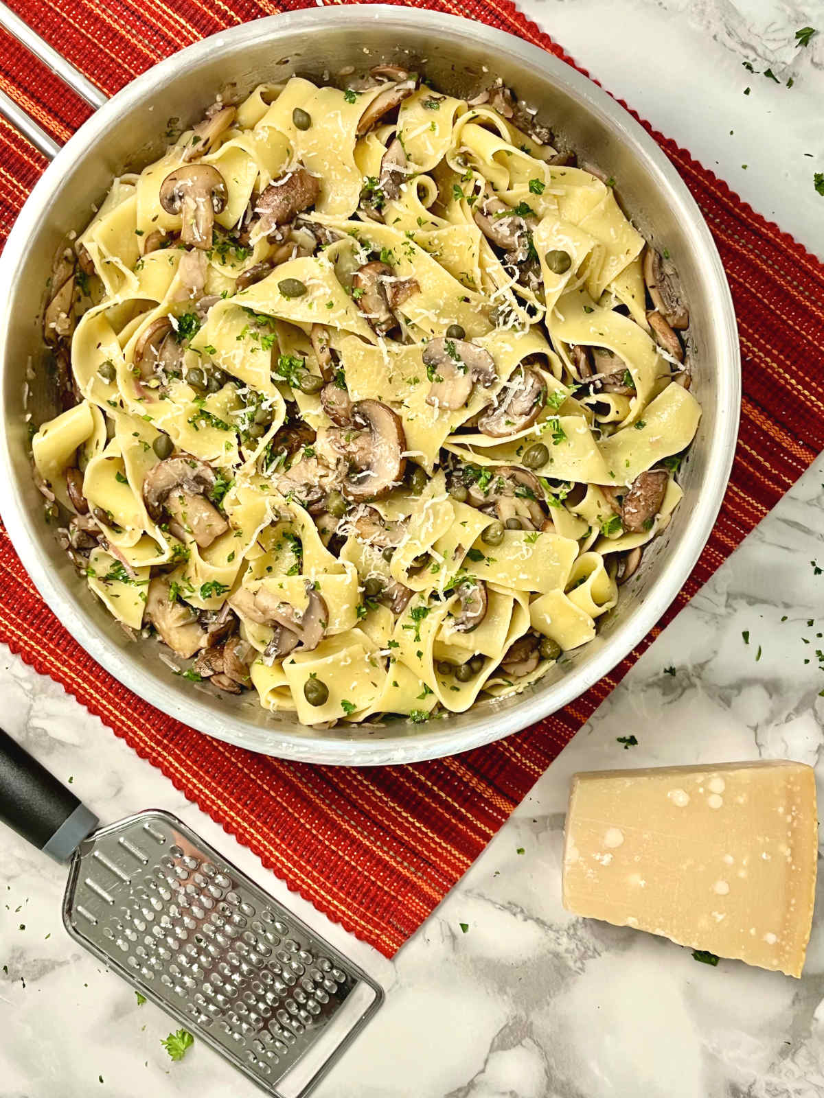 Mushroom Pappardelle in a pan with a block of cheese and a grater on the side