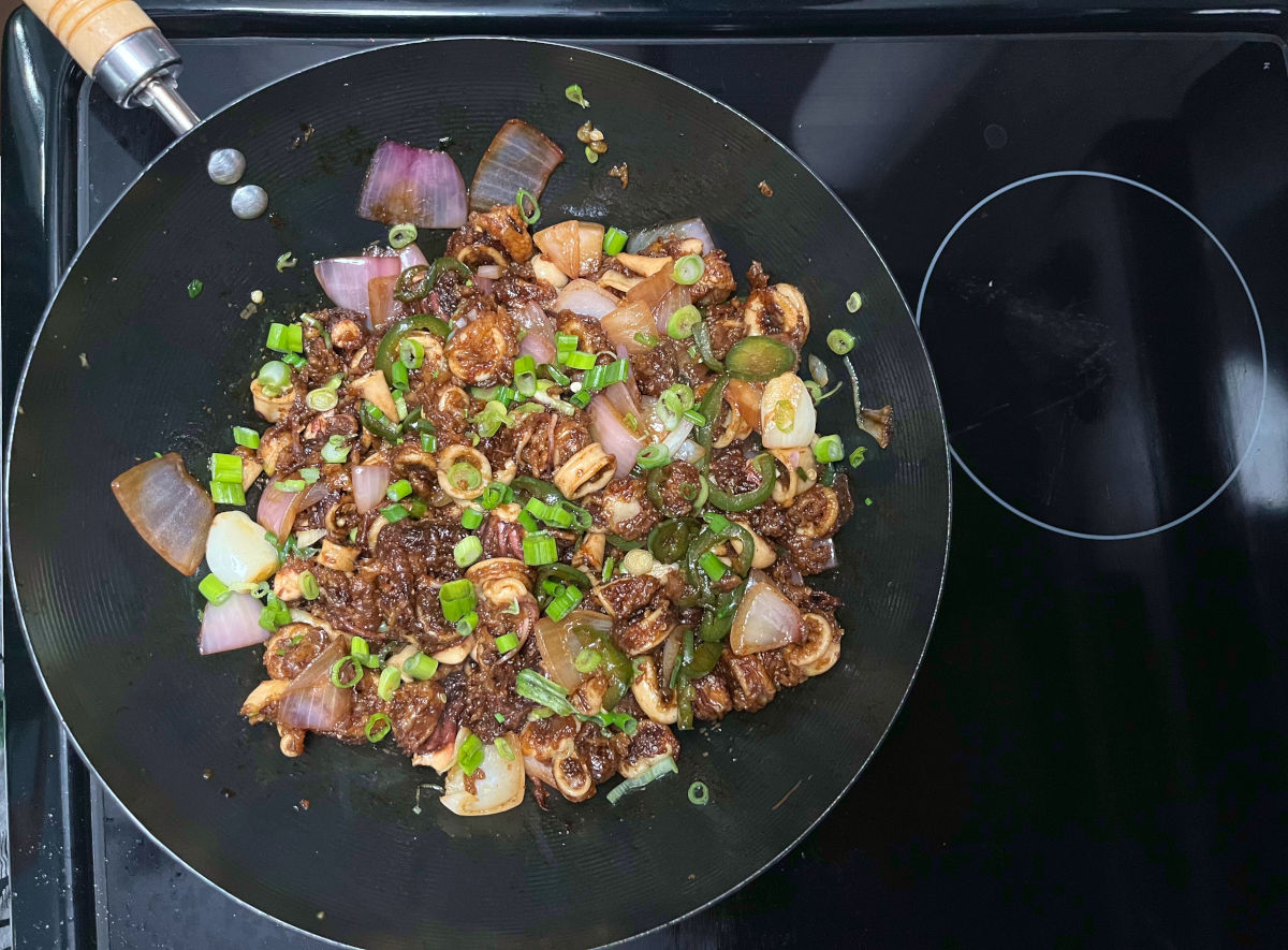 all ingredients in a wok topped with sliced green onions