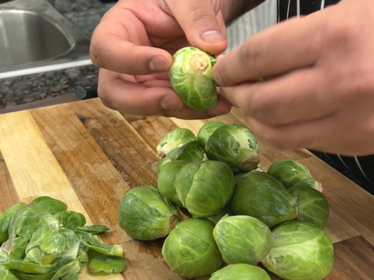 cook is cleaning brussels sprouts on a cutting board