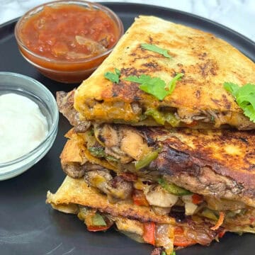 slices of jerk chicken quesadilla on a plate with bowls of salsa and sour cream on the side