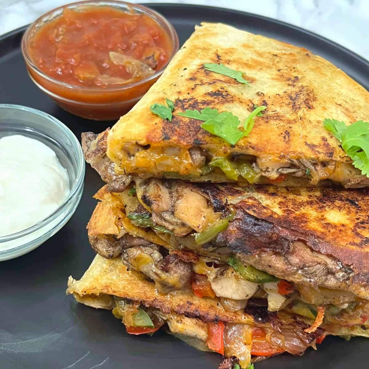 slices of jerk chicken quesadilla on a plate with bowls of salsa and sour cream on the side