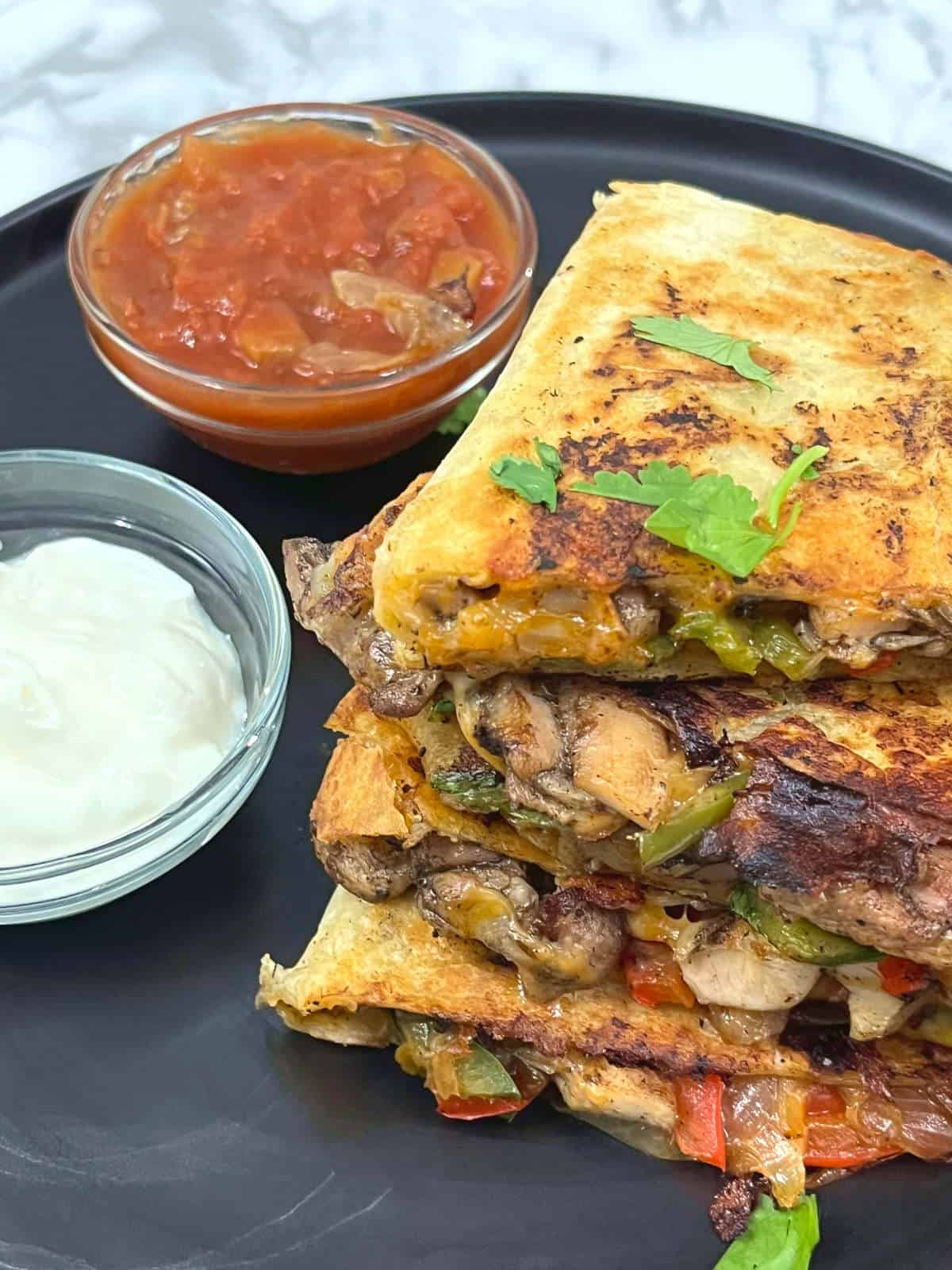 slices of jerk chicken quesadilla on a plate with bowls of salsa and sour cream on the side