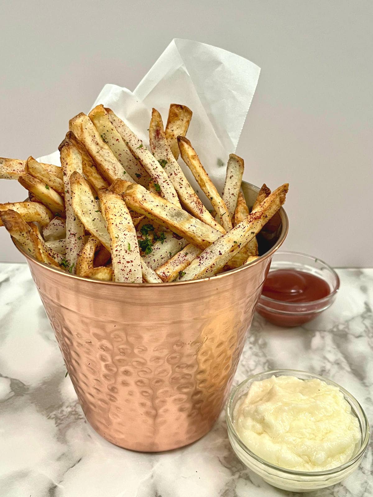 sumac fries in a bucket with toum and ketchup on the side